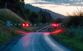 Ein Bahnübergang mit gesenkten Schranken und rot blinkenden Warnlichtern in der Abenddämmerung