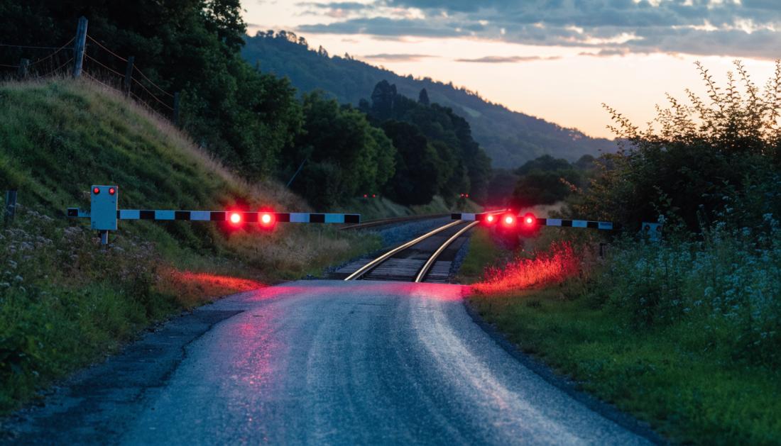Ein Bahnübergang mit gesenkten Schranken und rot blinkenden Warnlichtern in der Abenddämmerung