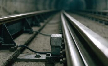 Nahaufnahme einer seitlichen Stromschiene neben den Fahrschienen in einem dämmrigen Tunnel