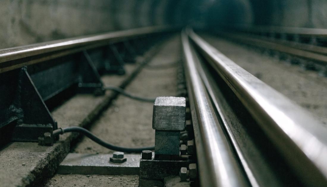 Nahaufnahme einer seitlichen Stromschiene neben den Fahrschienen in einem dämmrigen Tunnel