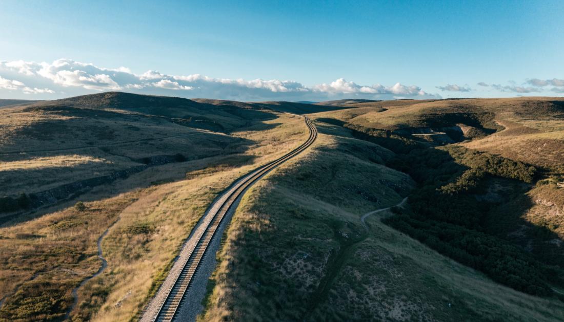 Eine Bahnstrecke schwingt sich elegant durch eine hügelige Landschaft, aus der Vogelperspektive fotografiert