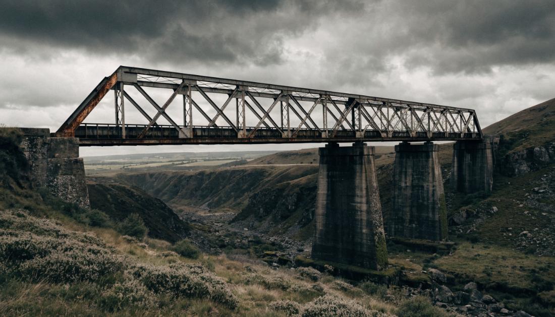 Eine alte verwitterte Eisenbahnbrücke mit sichtbarem Rost unter bewölktem Himmel