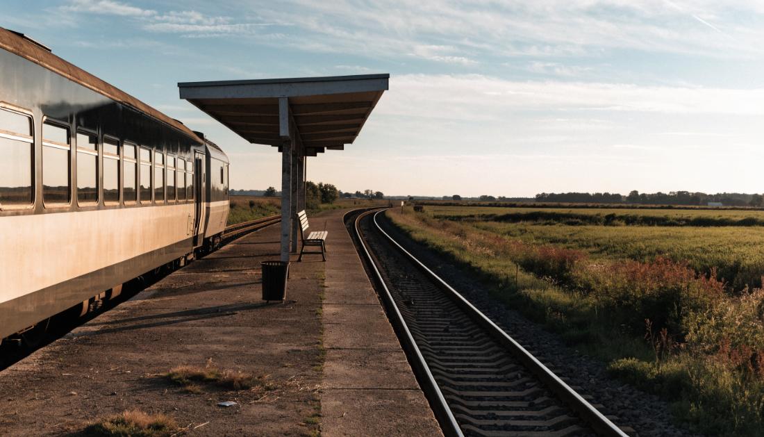 Ein kleiner ländlicher Bahnsteig inmitten offener Landschaft mit einem wartenden Regionalzug