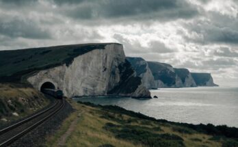 Ein Zug fährt in ein langes Tunnelportal in einer Kreidefelsenlandschaft nahe dem Meer