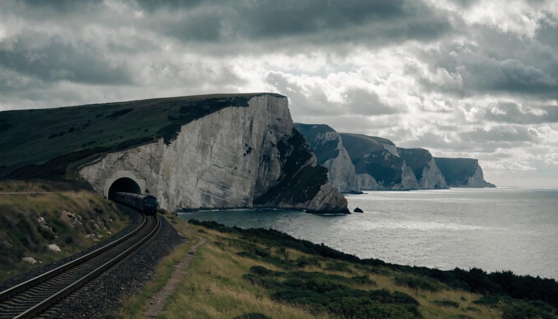 Ein Zug fährt in ein langes Tunnelportal in einer Kreidefelsenlandschaft nahe dem Meer