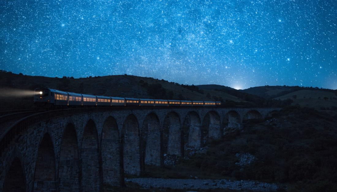 Ein langer Nachtzug überquert ein Viadukt unter tiefblauem Sternenhimmel