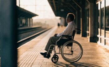 Eine Person im Rollstuhl wartet ruhig auf einem Bahnsteig im warmen Tageslicht