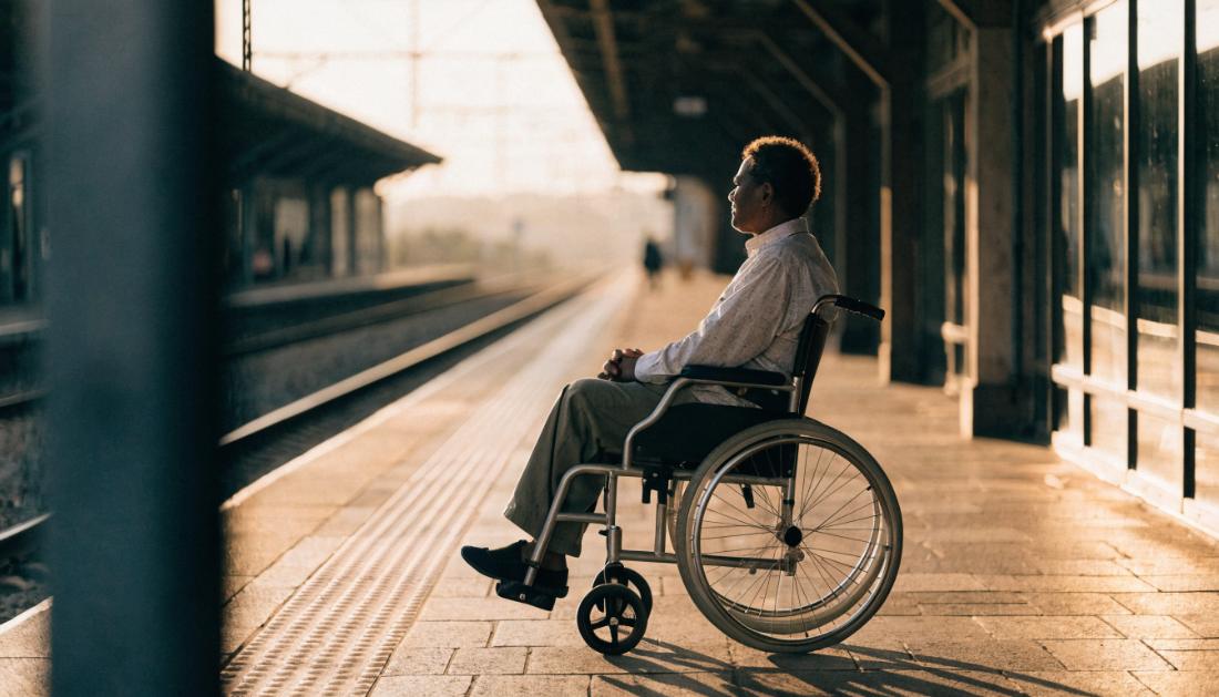 Eine Person im Rollstuhl wartet ruhig auf einem Bahnsteig im warmen Tageslicht