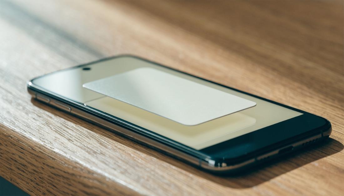 Eine unbeschriftete Zahlungskarte liegt auf einem Smartphone auf einem Holztisch
