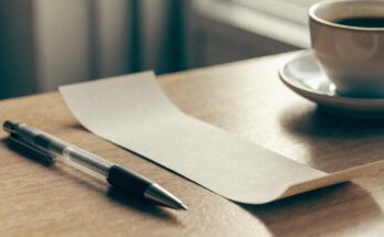 Ein schlichtes Papierticket liegt auf einem Schreibtisch neben Stift und Kaffeetasse