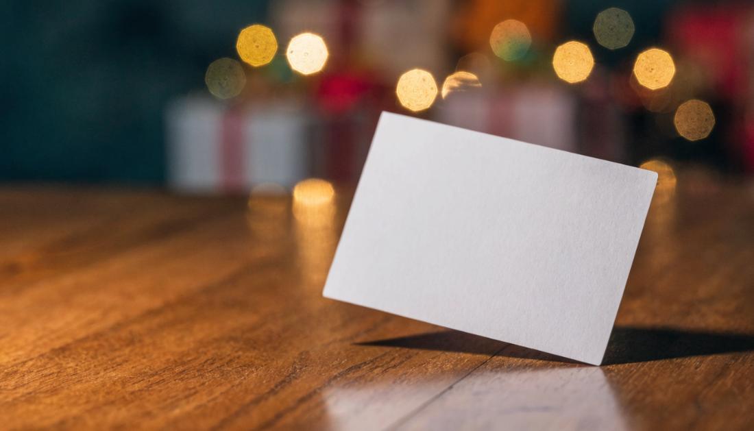Eine unbeschriftete Geschenkkarte liegt auf einem Holztisch mit warmen unscharfen Lichtern im Hintergrund