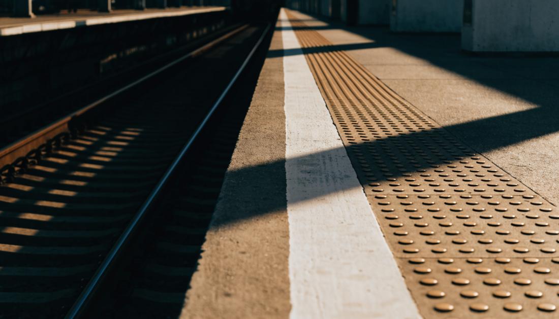 Nahaufnahme einer aufgemalten Sicherheitslinie an der Kante eines Bahnsteigs mit Riffelstreifen