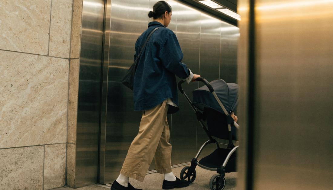 Ein Elternteil schiebt einen Kinderwagen in einen Bahnhofsaufzug