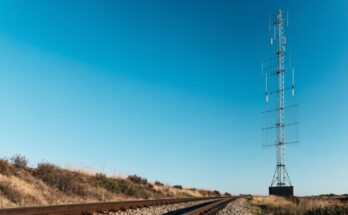 Ein Funkmast neben Bahngleisen vor weitem Himmel