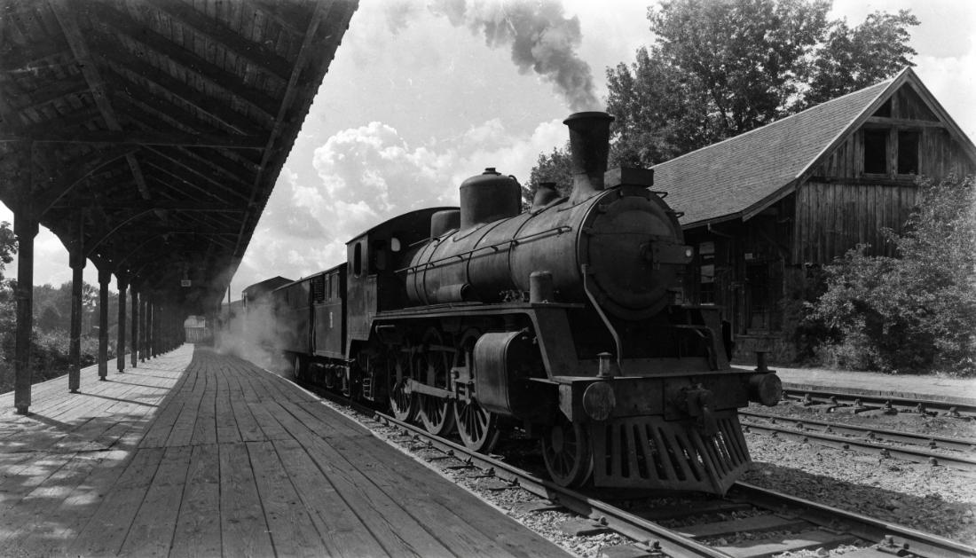 Eine historische Bahnszene mit einer alten Dampflokomotive an einem Bahnsteig