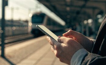 Reisender schaut am Bahnsteig auf sein Handy mit dem DB Navigator