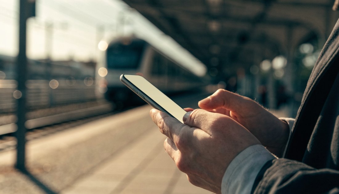 Reisender schaut am Bahnsteig auf sein Handy mit dem DB Navigator