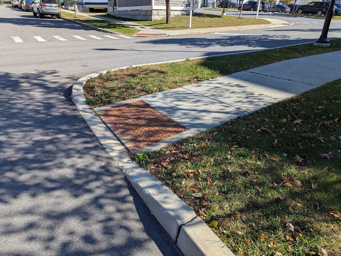 Long gradual sidewalk ramp to tactile paving and curb cut in Colchester