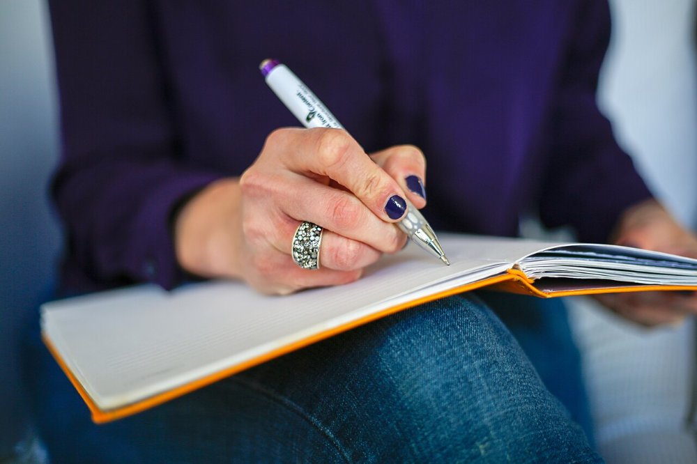 Person schreibt mit einem Stift in ein Notizbuch am Schreibtisch