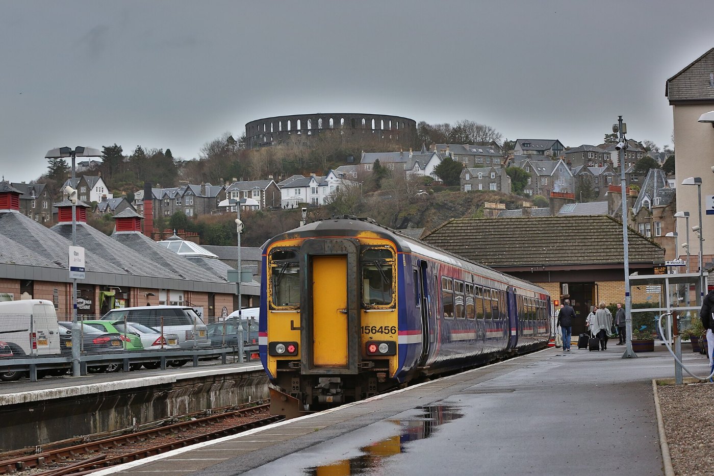 A Class 156 diesel train at Oban train station with McCaigs Tower in the